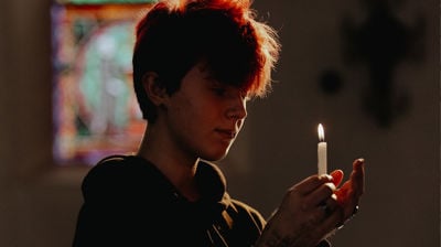 Ung gutt står inne i et kirkerom med et stearinlys i hendene. Han ser på lyset og smiler. 