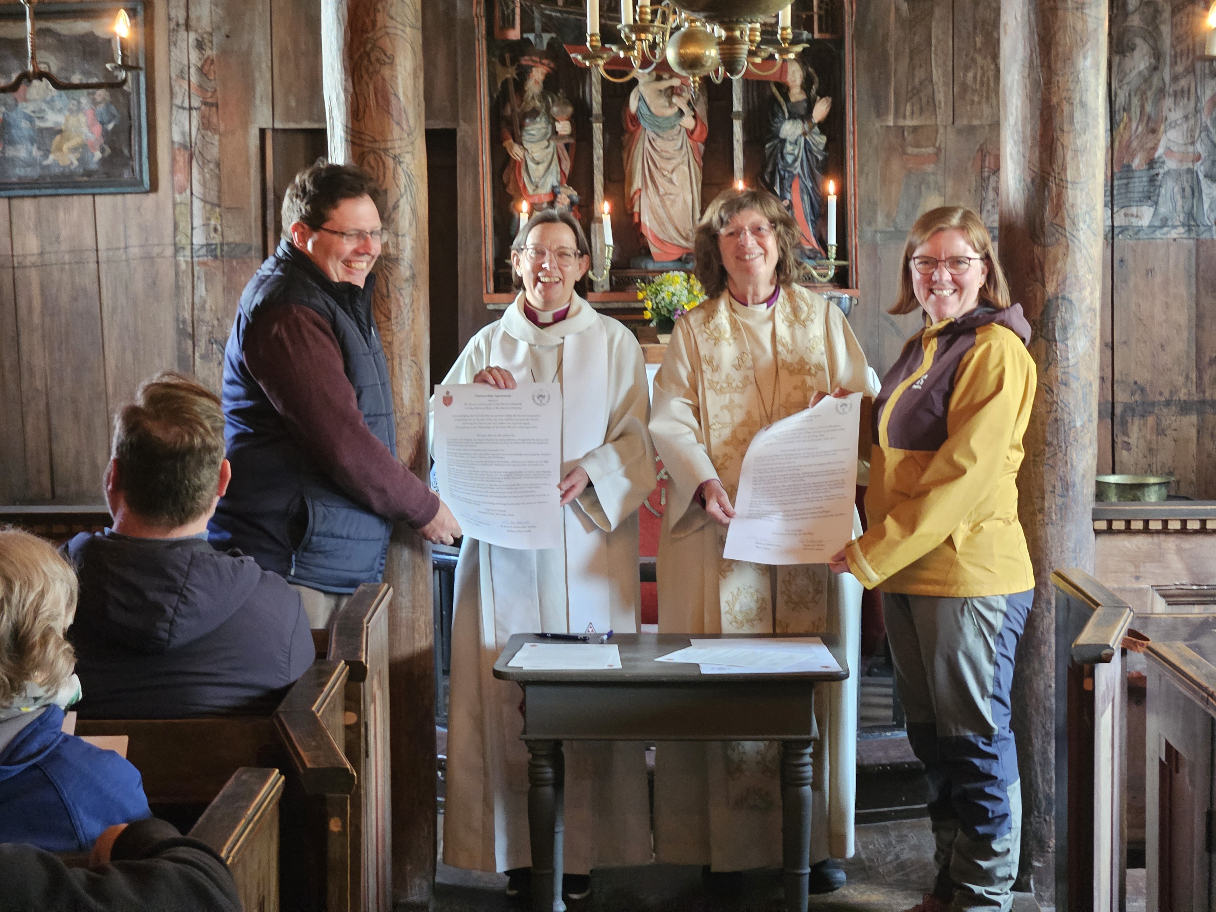 Dean Lee Batson, bishop Helen-Ann, biskop Ingeborg Midttømme, domprost Grethe L. Johnsen viser fram de signerte avtalene foran alteret i Grip stavkirke. 