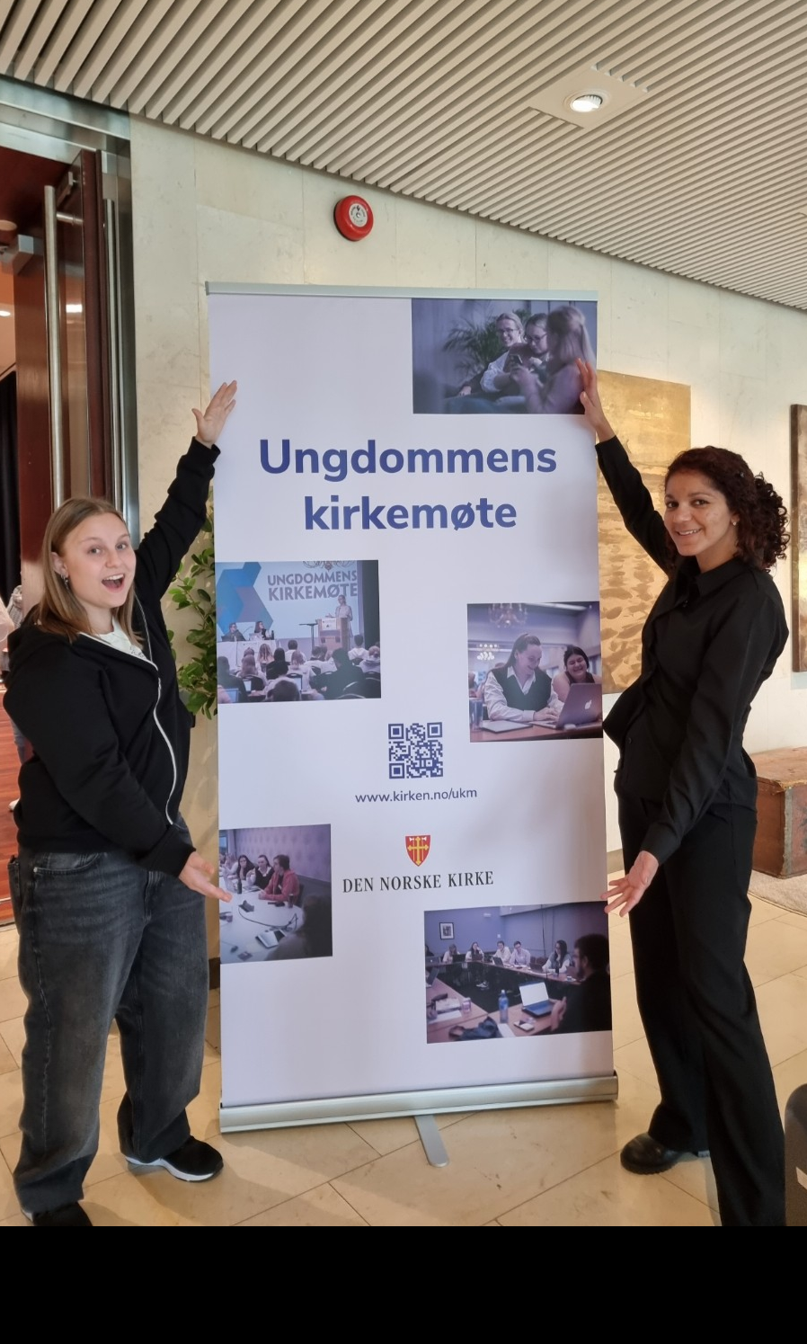 Helene Viken Hovlan og Sylviane Jacques Denis deltok på UKM frå Møre. Synstolkning: bilete av Helen og Sylviane som står foran eit banner for UKM. 