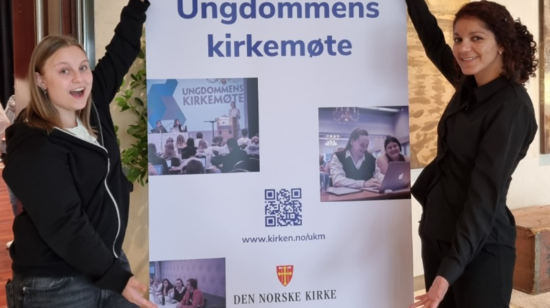 Helene Viken Hovlan og Sylviane Jacques Denis deltok på UKM frå Møre. Synstolkning: bilete av Helen og Sylviane som står foran eit banner for UKM.