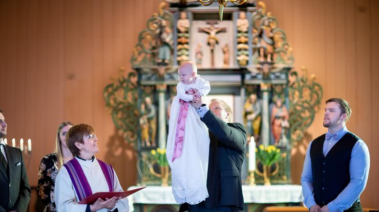 Dåpsbarn med dåpskjole løftes opp foran menigheten. Foto: Den norske kirke / Bo Mathisen 