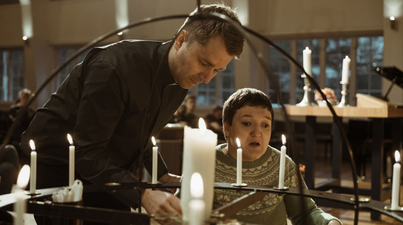 En diakon hjelper en person med å tenne et lys i lysgloben.