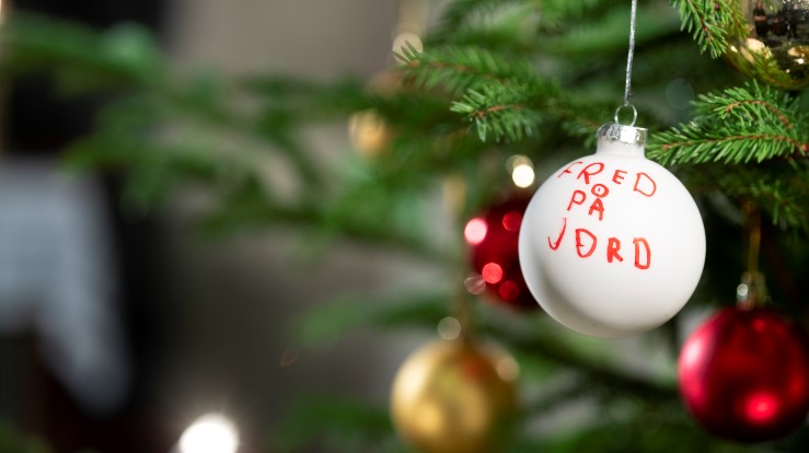 Ei julekule henger på juletreet. På kula er det skrevet med rød tusj: Fred på jord. 