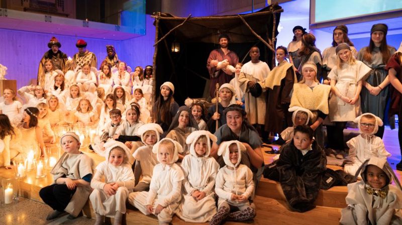 Levende julekrybbe med sauer, gjetere, engler, Josef, Maria og Jesusbarnet. Alle står oppstilt fremfor en stall.