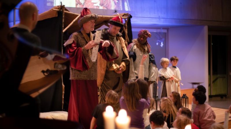 Levende julekrybbe. De tre vise menn står på scenen. Mange barn ser på.