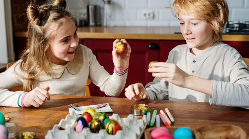 Gutt og jente som sitter og maler på påskeegg