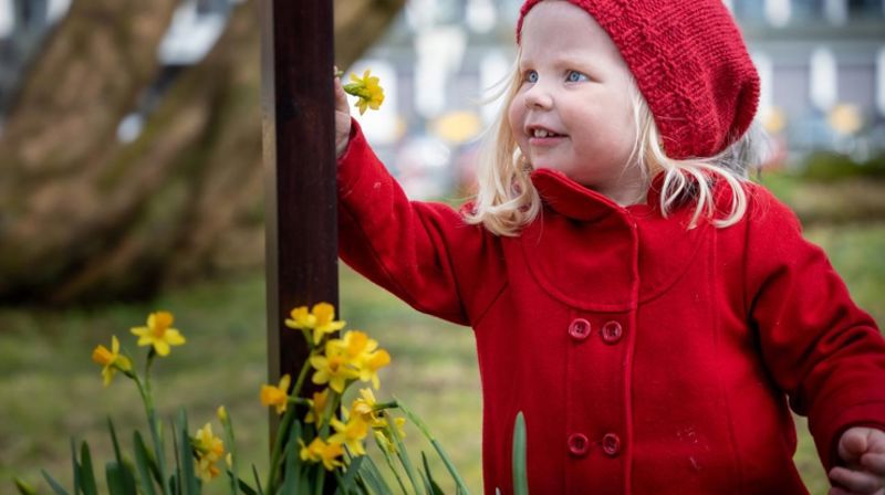 En jente setter en påskelilje opp på et kors. Hun er rundt 4 år gammel, er utendørs og smiler