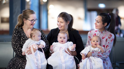 Tre mødre holder hvert sitt dåpsbarn trygt inntil seg. Det er tydelig på bildet at det er glede når det er dåp i kirken!