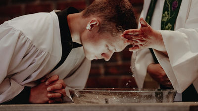 En ungdom som lener seg over døpefonten får vann i pannen av presten som døper ham.