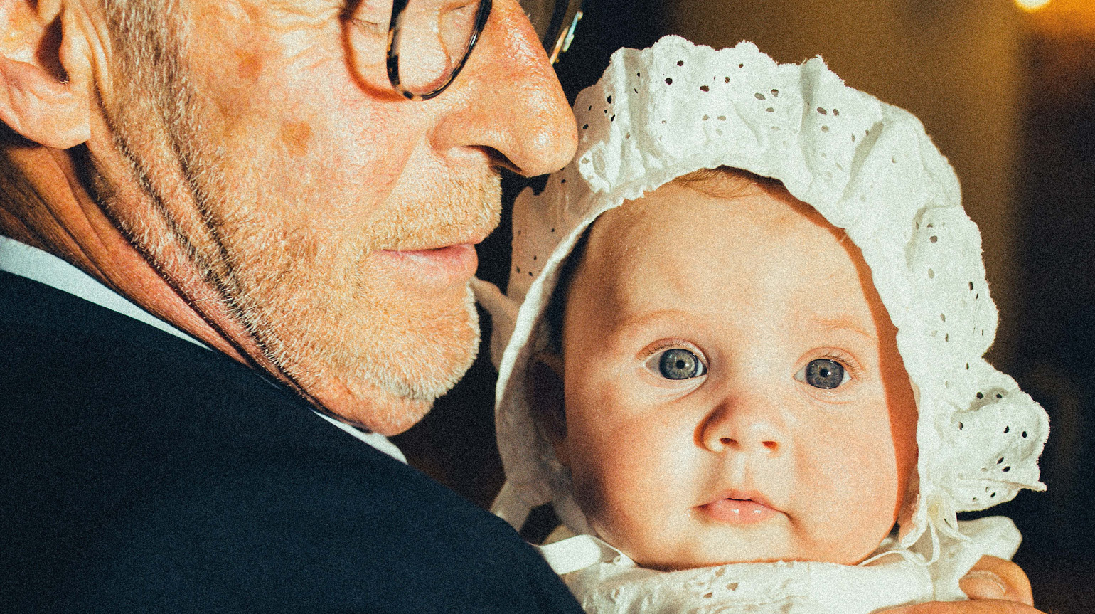 En eldre mann som holder et dåpsbarn med dåpslue