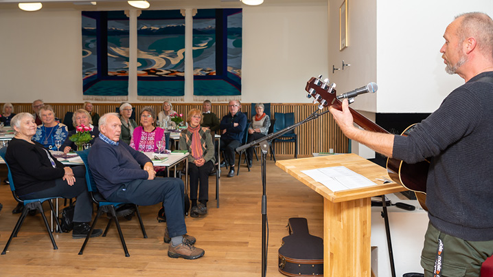 En mann spiller gitar og synger for en gruppe mennesker i kirken. 