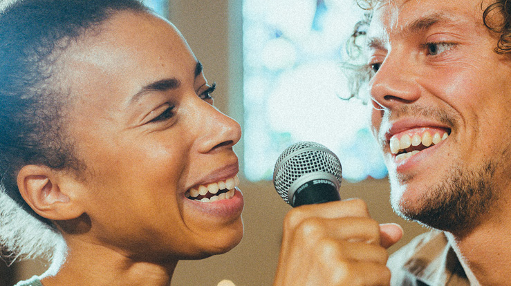 To personer står tett og synger i en mikrofon i et kirkerom