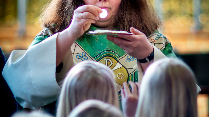 En prest holder opp en oblat, brødet i nattverden, mens en kø har gjort seg klar for å ta imot og spise, under nattverdsutdelingen i gudstjenesten.