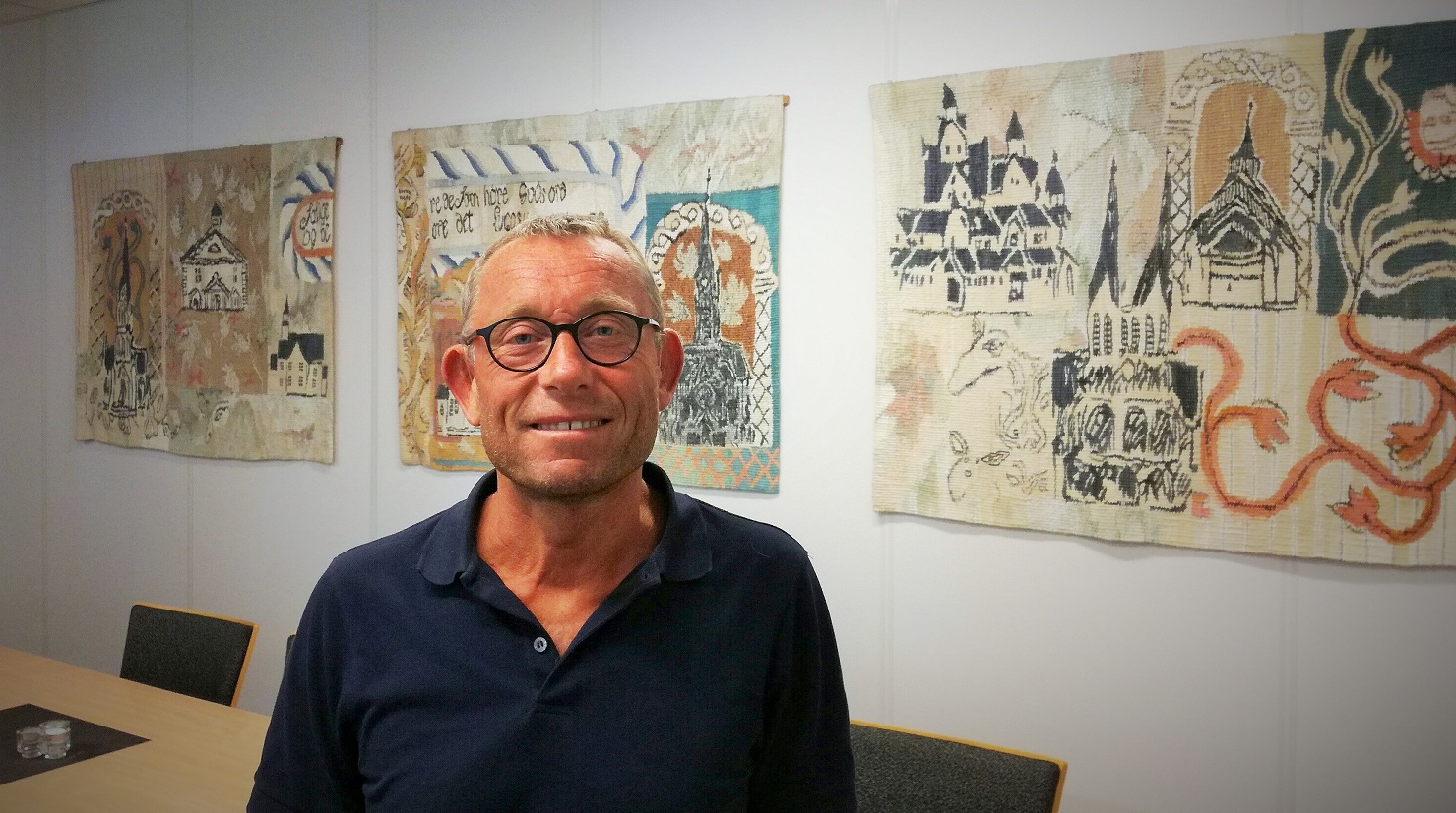 Steinar Skomedal i møterommet på bispedømmekontoret i Kristiansand der bilder av Else Marie Jakobsen pryder veggen. Foto Dag A. Kvarstein