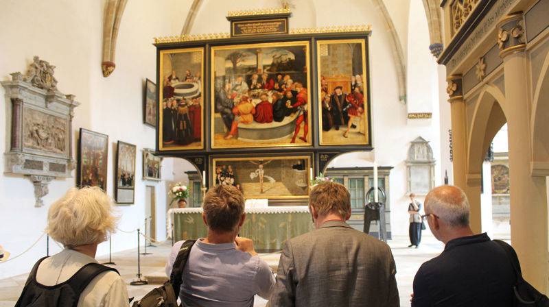 Biskopen viste i preika si til altartavla i Martin Luther si kyrkje i Wittenberg, Stadtkirche St. Marien. Altartavla viser nådemidla og er malt av Lucas Cranach.