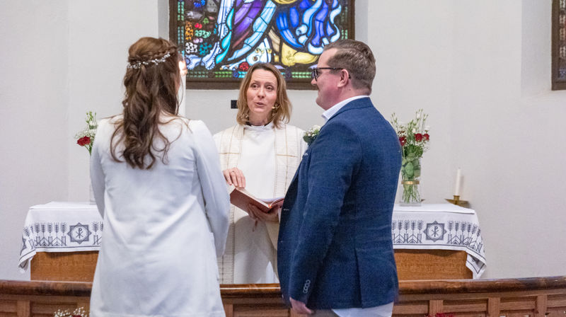 Synstolkning: I 2023 valgte blant andre Bjørg og Are denne rammen for sitt bryllup. I årene som kommer kan de dermed bruke kjærlighetens dag til å feire bryllupsdag. Her er de sammen med prost Kjerstin Jensen i Ås kirke. Foto: Inger Eide Nordseth