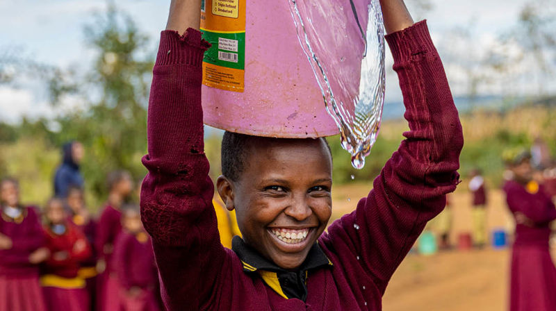 Foto: Kirkens nødhjelp. Gutt som holder en bøtte med rent vann på hodet.