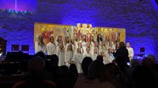 Korsangere i hvite kapper foran Holmen kirkes altertavle og blå fondvegg.