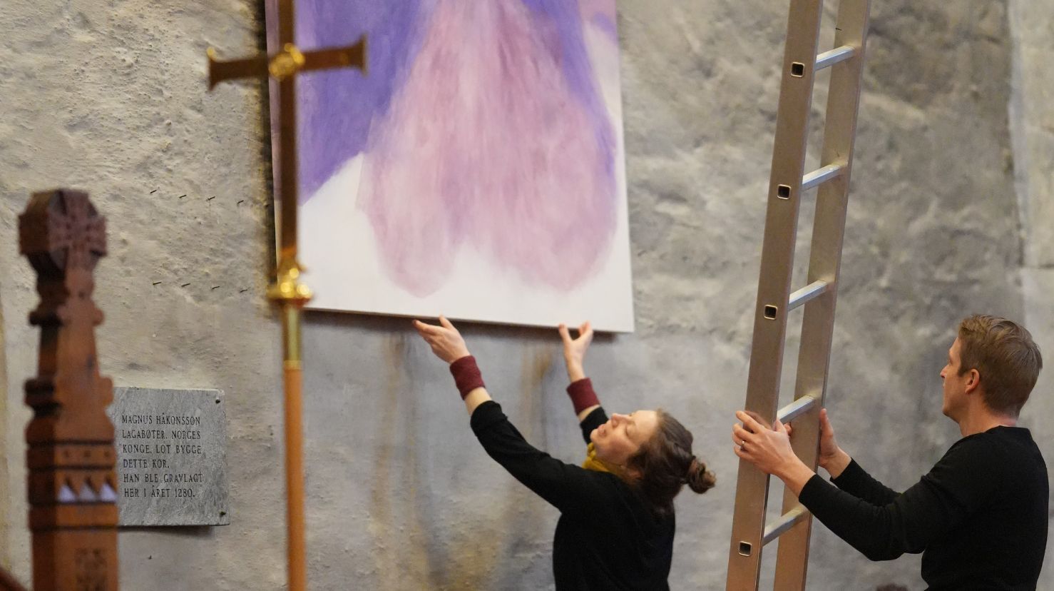 Kunstner Gunhild Sannes og domkantor Kjetil Almenning passer på at bildet henger greit på veggen i Bergen domkirke.
