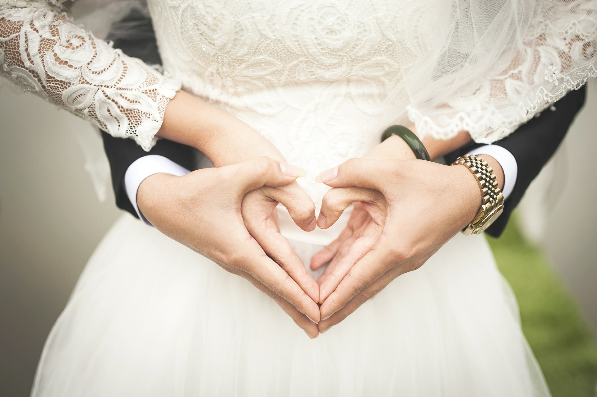 Ektepar i bryllupsstasen holder hendene frem i hjerteform. Utsnitt av hender og midje.