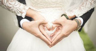Ektepar i bryllupsstasen holder hendene frem i hjerteform. Utsnitt av hender og midje.