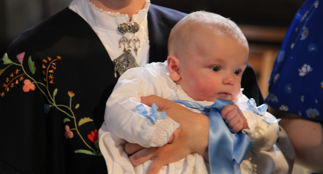 Dåpsbarn i hvit kjole holdt av forelder.