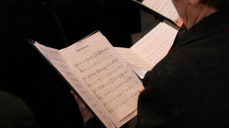 Utsnitt av ei gruppe menneske med noteark i hendene