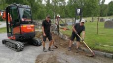 Kirketjenerne Terje Hognestad og Jan Myrvold graver frem igjen kantestein utenfor Moen kirke og gravplass. Et eksempel på sommeroppgaver ute (foto: Knut Bøe).