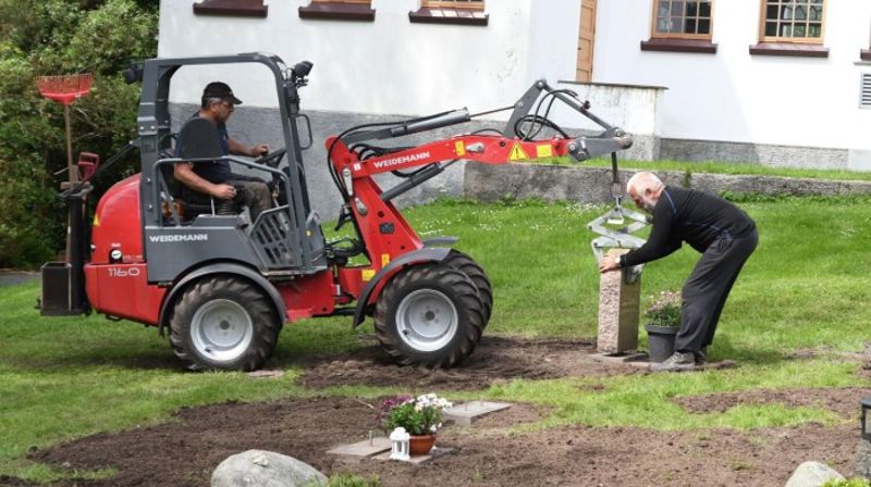 Ferdig: Mandag ble de siste gravsteinene løftet på plass etter sju års arbeid med cirka 2.500 gravsteiner på kommunens kirkegårder. Her ser vi gravplass- og kirkebyggsjef Bjørn Undheim med steinen og Helge Flaath i traktoren.