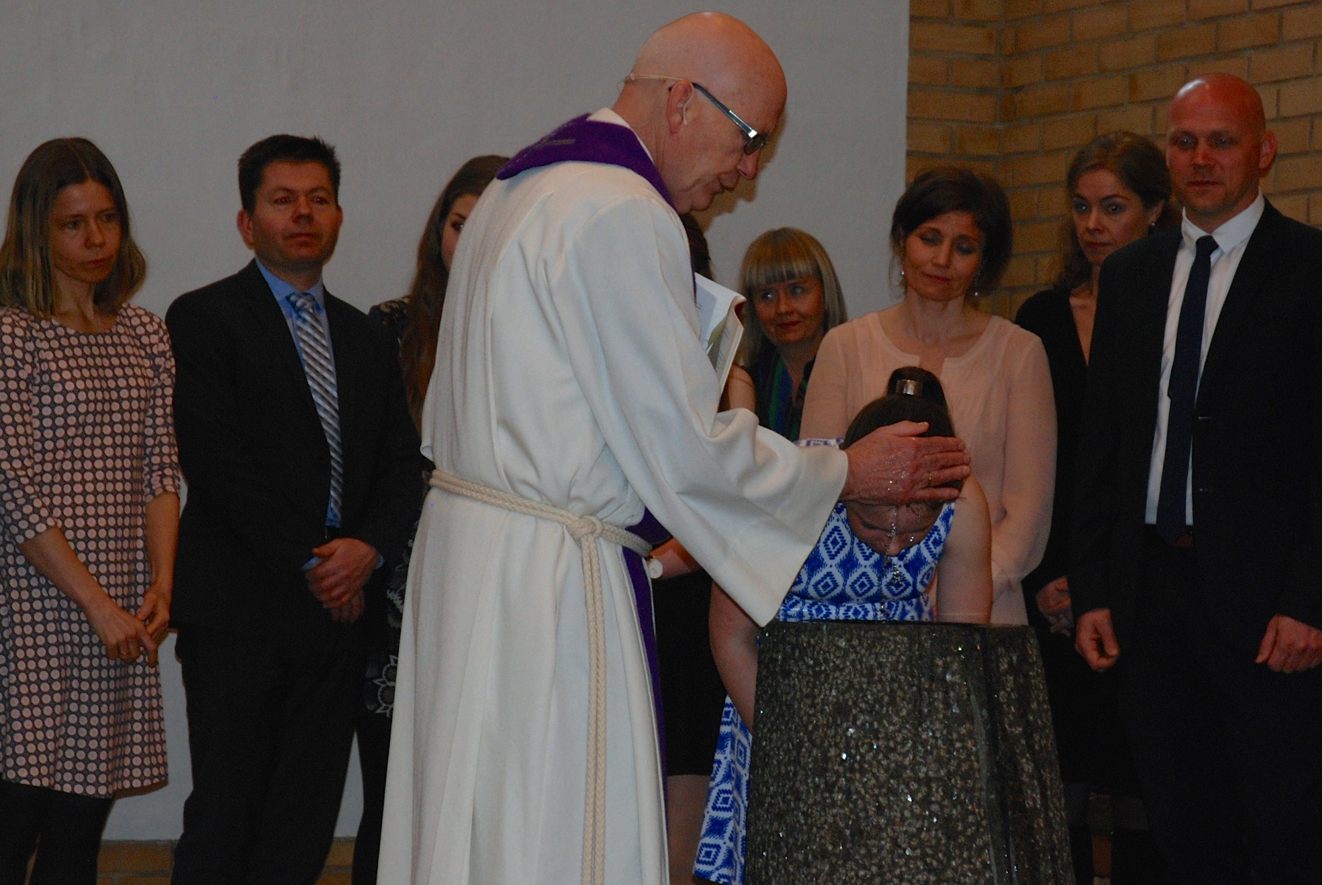 Familie og faddere står rundt mens Jorunn bøyer seg over døpefonten.