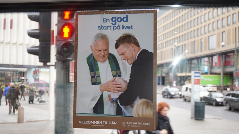 En av dåpsplakatene som fyller bybildet. Dette er tatt på 37 bussen, og vi ser sokneprest Espen Feilberg Jacobsen i Nordstrand med dåpsbarn og dåpspappa.