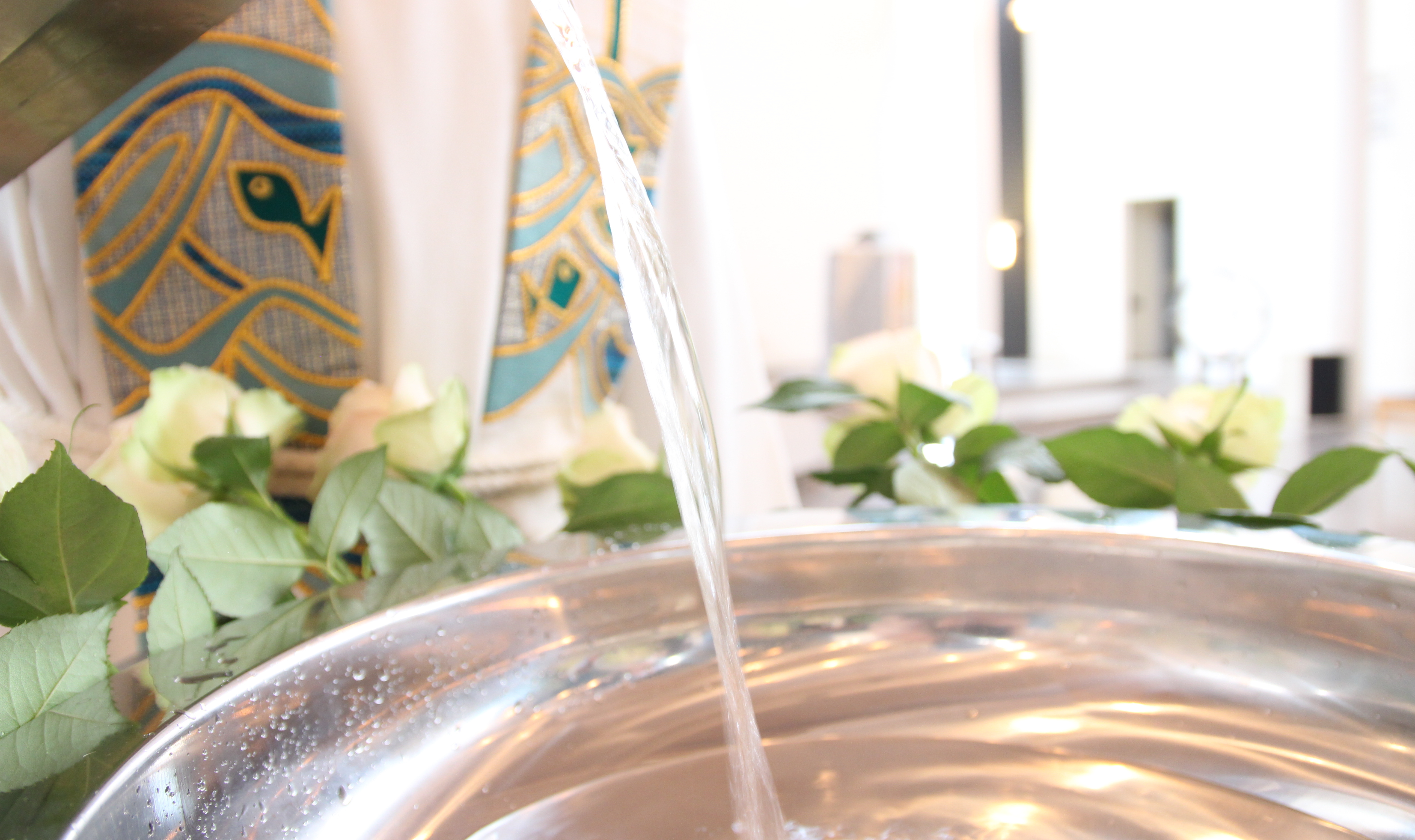 Presten heller vann oppi døpefonten, hvite roser er pyntet med rund sølvfatet.