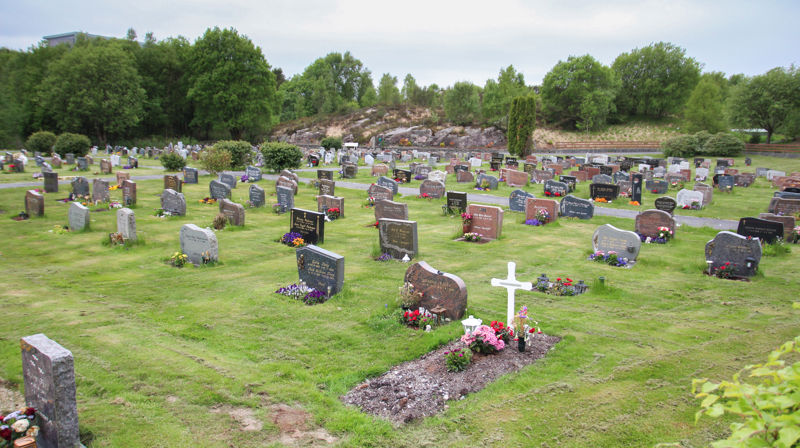 Oversikt over Straume gravplass med en relativt ny grav fremst, den har femdeles jord foran seg og roserbukett plasset oppå. Et hvit kors med navnet på bak rosene.