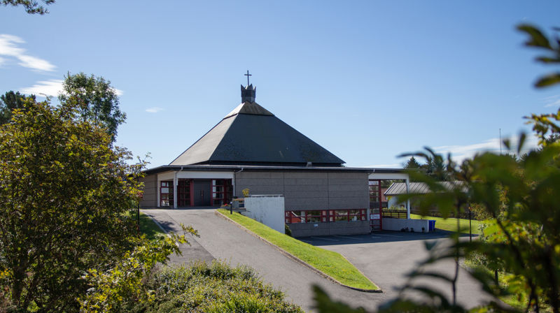 Landro kyrkje med trær og busker i forgrunnen, det er blå himmel.