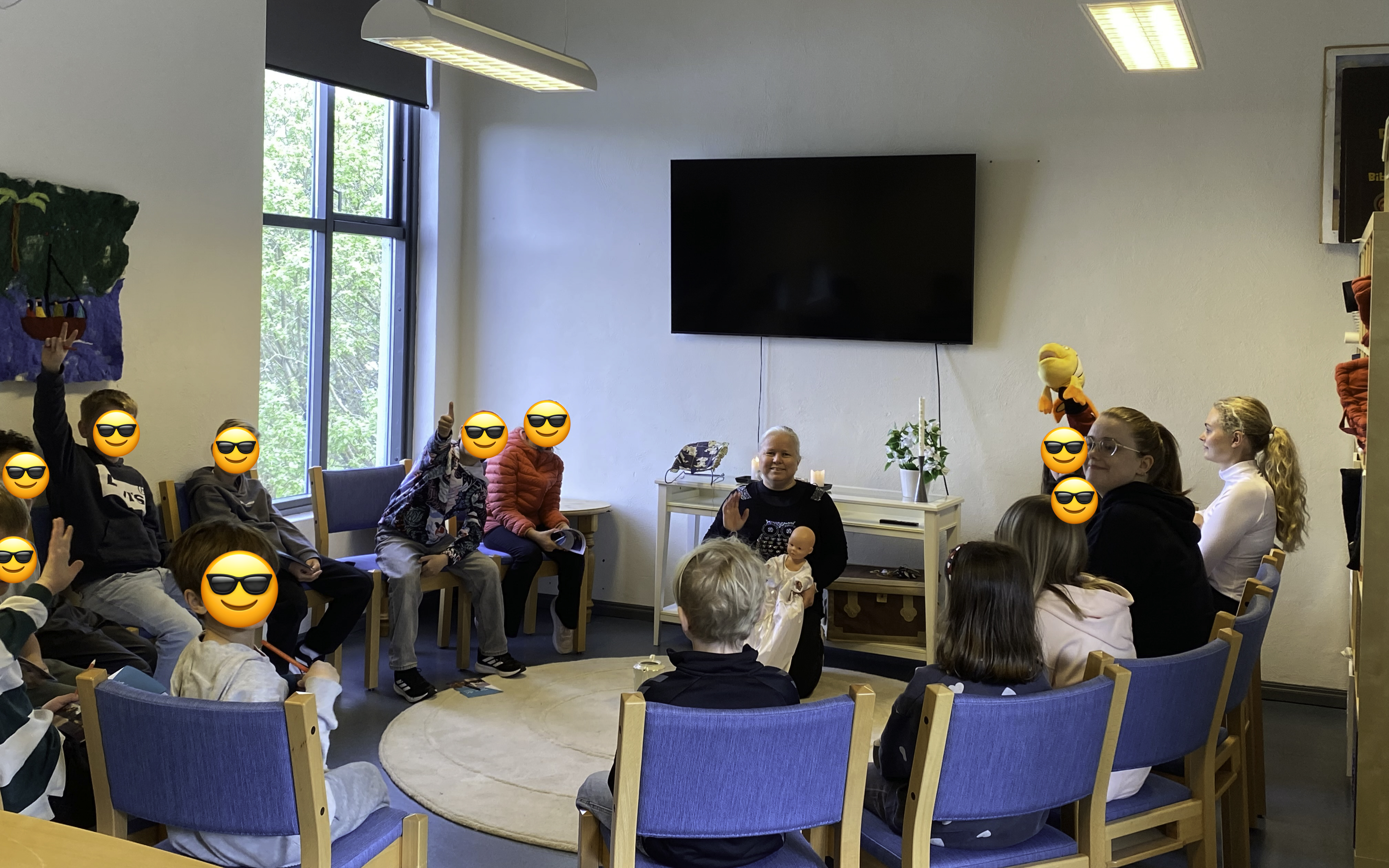 Barn og lærere sitter i en halvsirkel, ansiktene til barna er gjemt med en emoji med solbriller