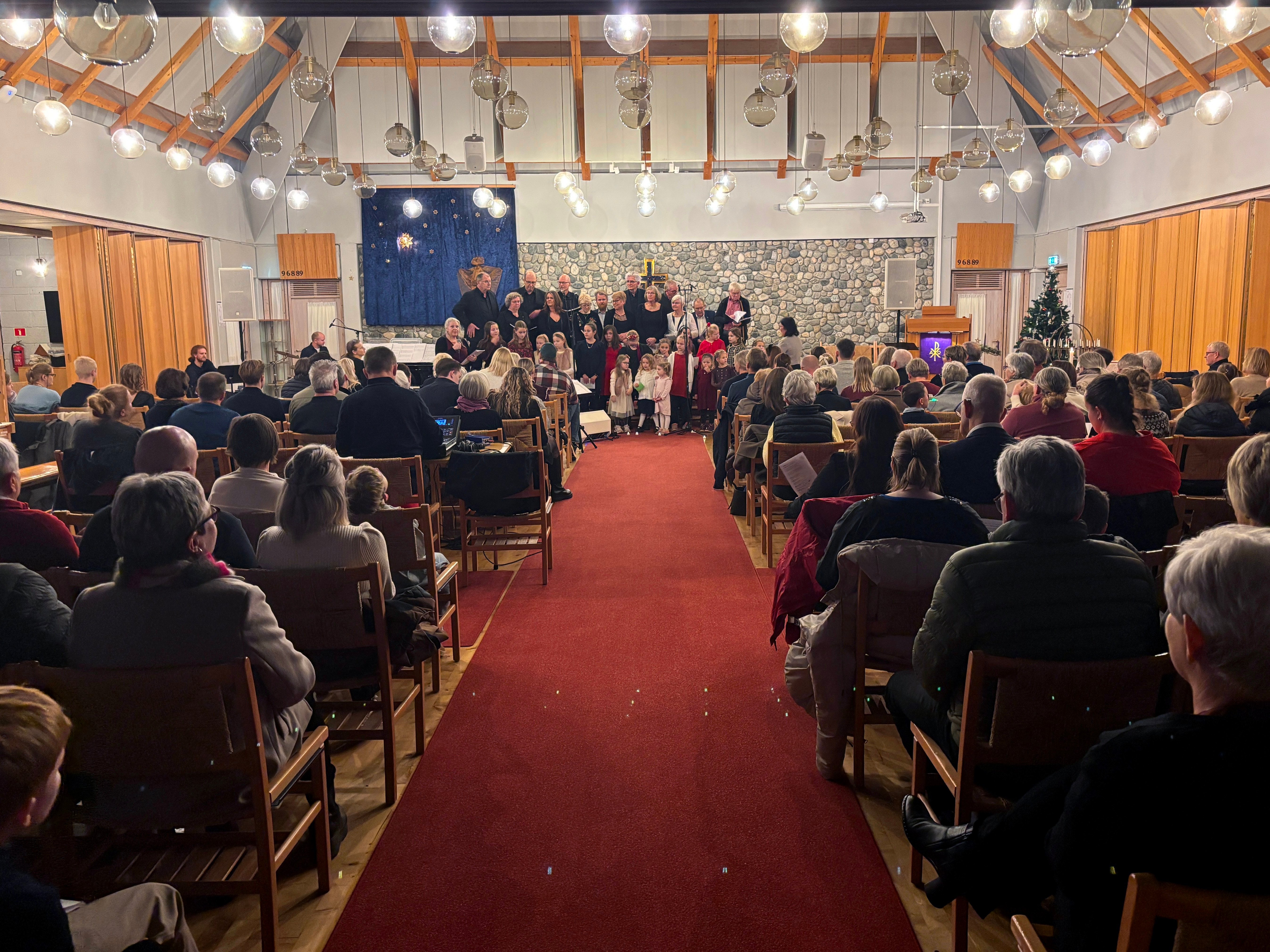 To kor, et barnekor, og et voksenkor, st&aring;r fremme i kirken. Stolene i kirkeskipet er full av menneske