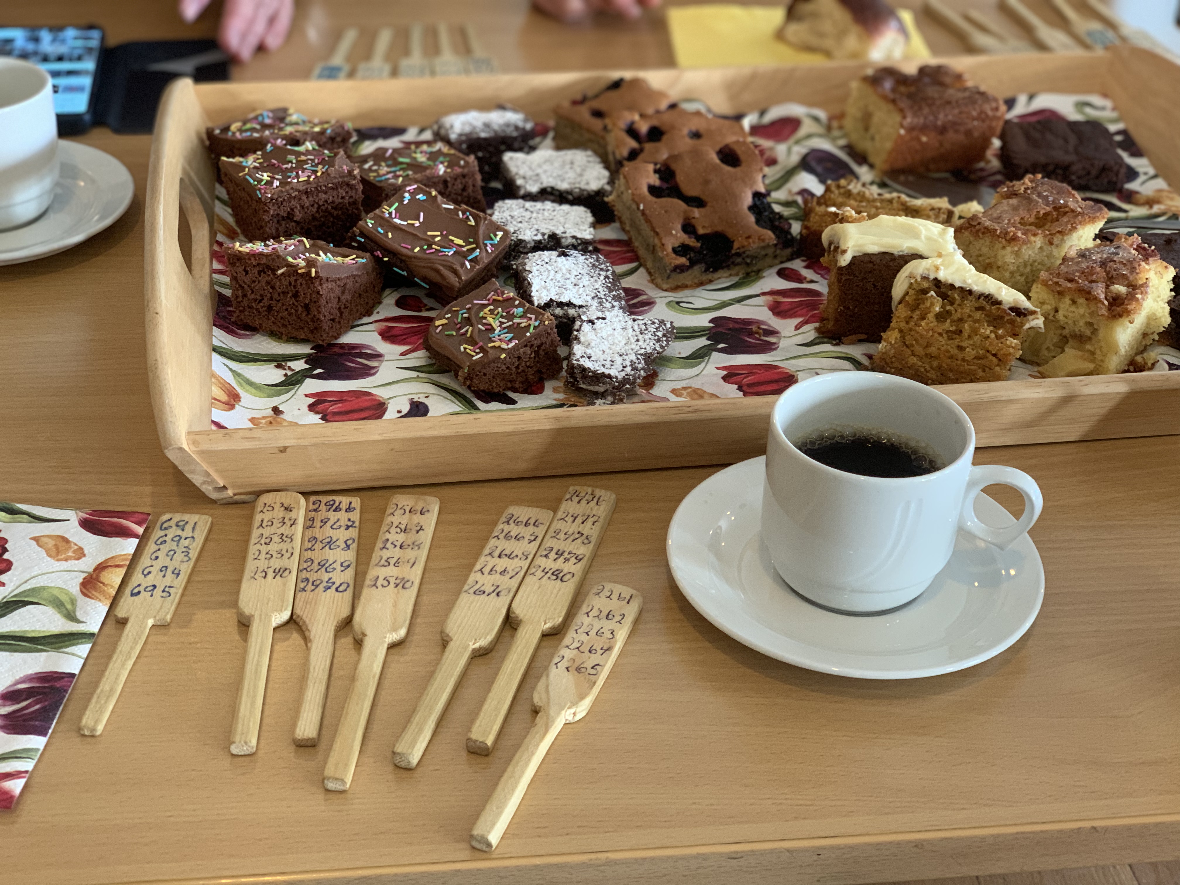 På et bord ligger basarårer, forskjellige kaker på et brett og en kopp kaffe