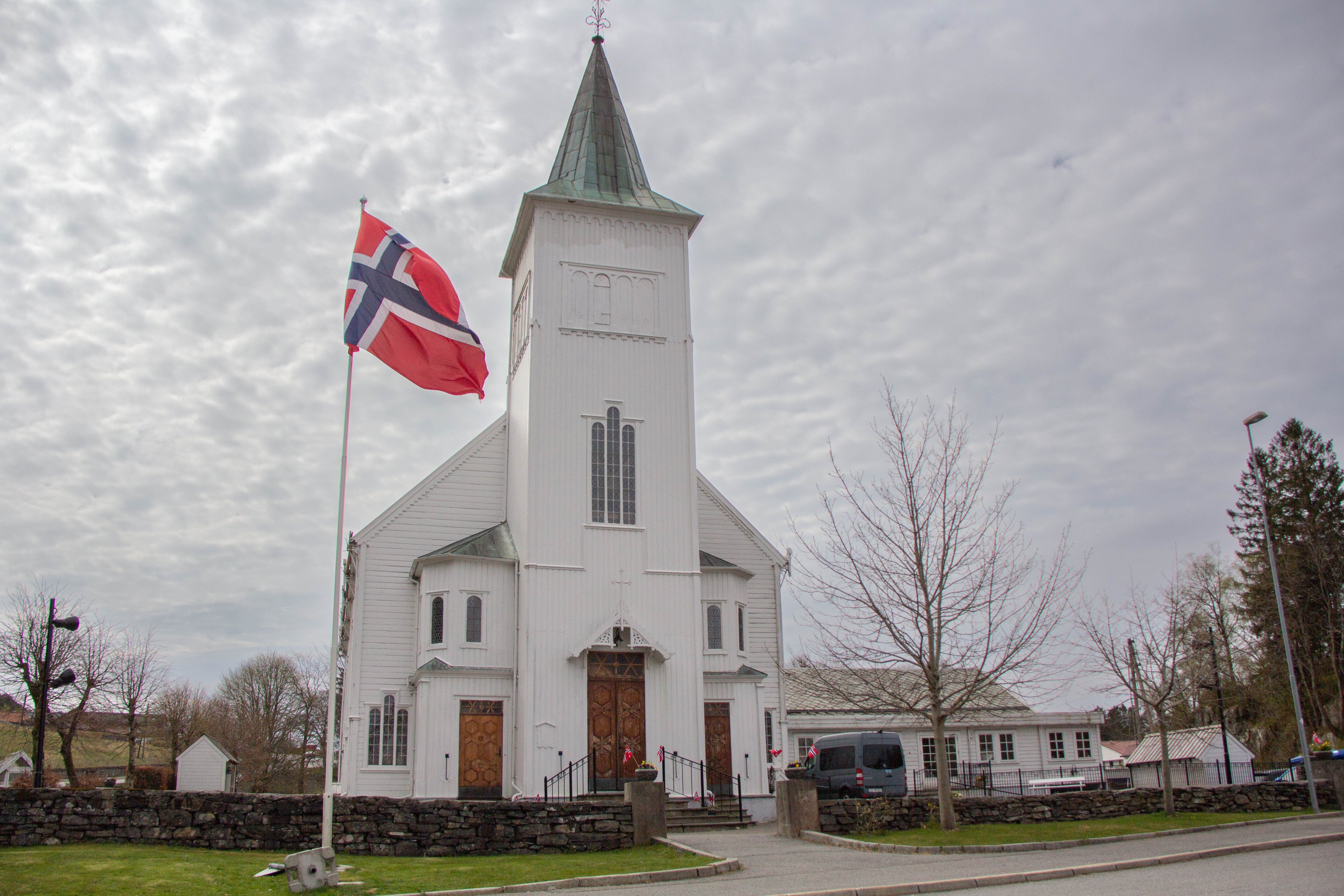 Fjell kyrkje i grå-ver, flagget er heist og det er pynta med småflagg i blomsterkassane