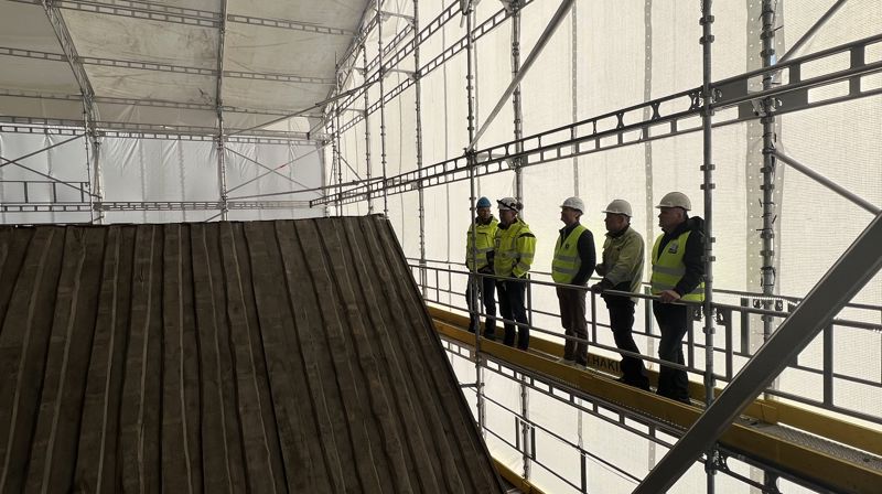 Arbeidarar står til venstre oppe i et stilas og ser på taket til kyrkja som er uten skifer.