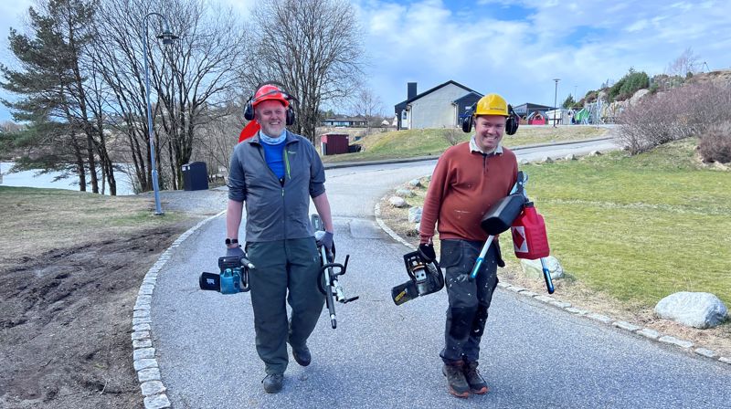 To menn kommer gående smilende, de har hjelm på hodet og verktøy i hendene