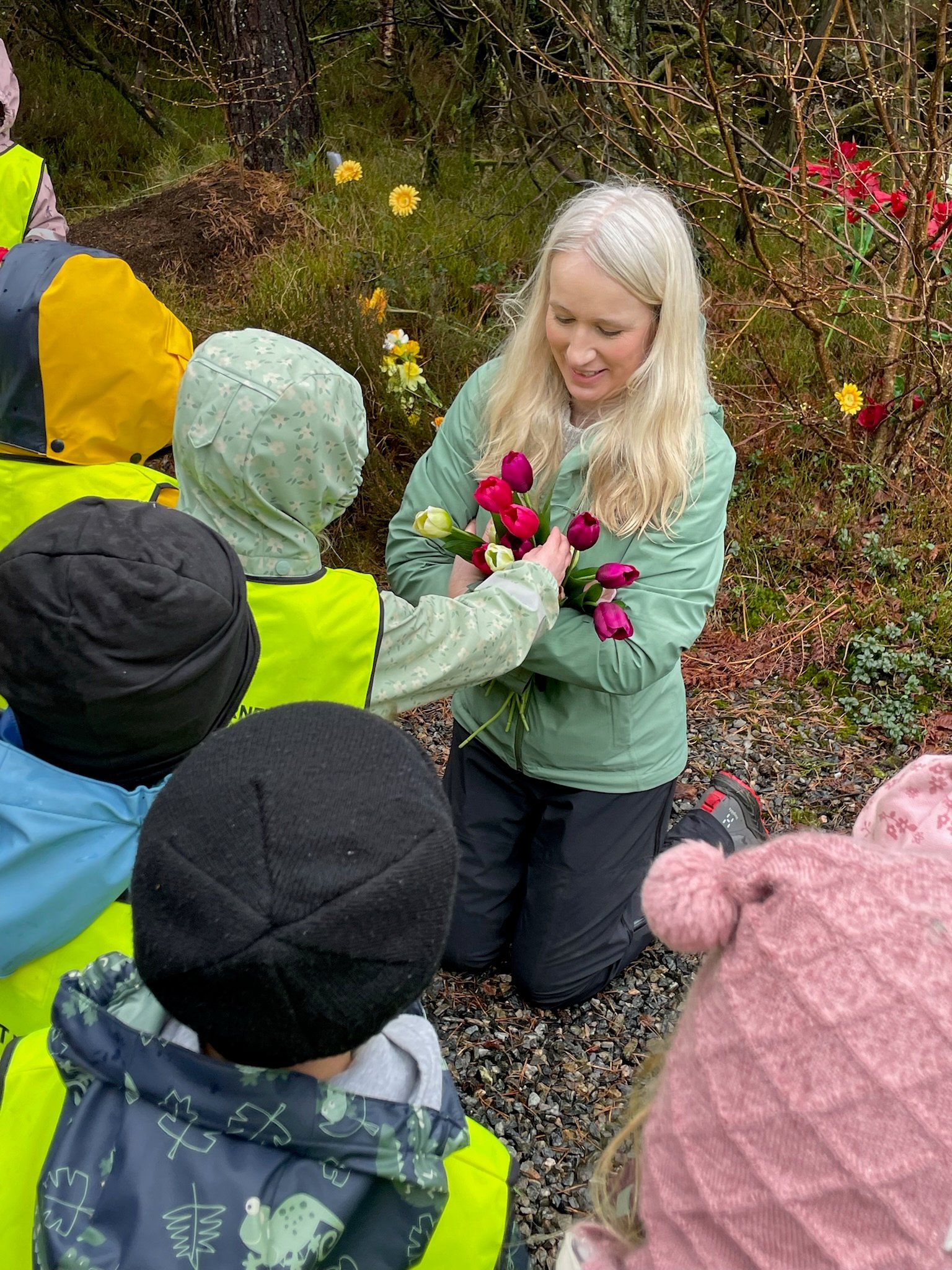 En dame sitter på huk og får fargerike tulipaner fra barnehagebarn