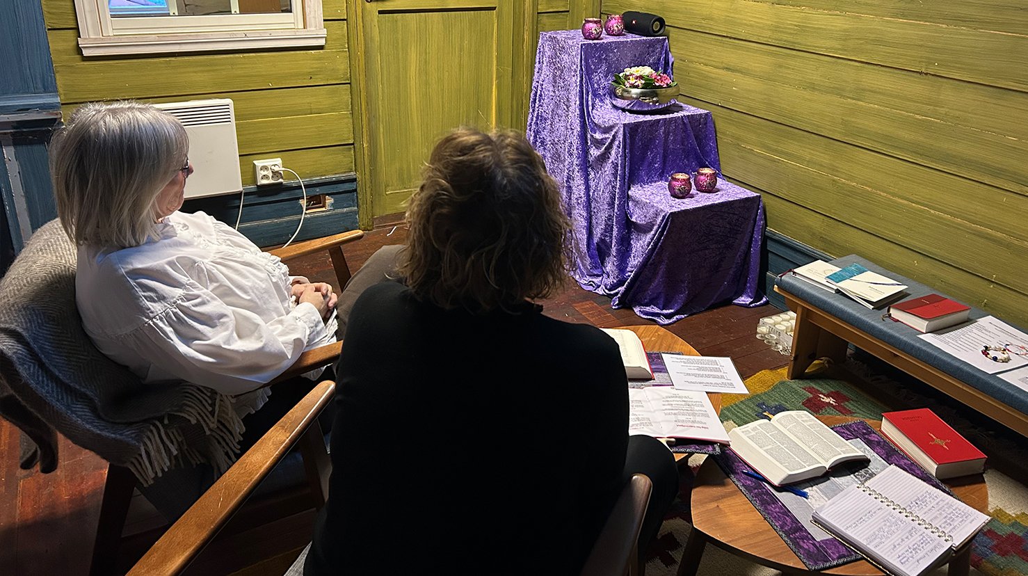 To damer sitter p&aring; hver sin stol inne i et rom og ber