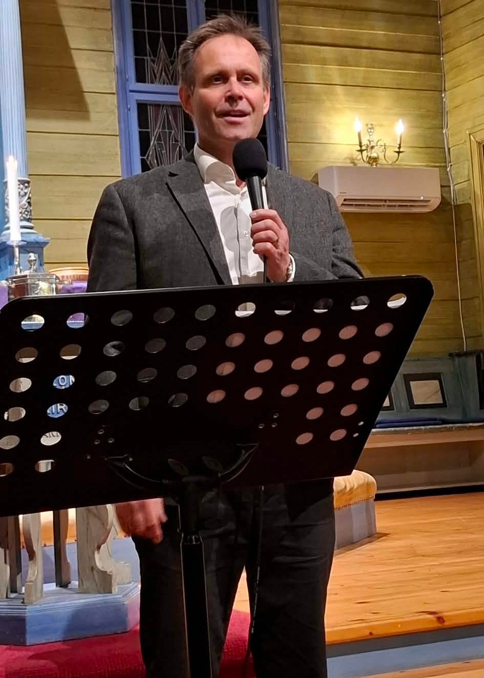 En mann st&aring;r fremme i en kirke og synger i mikrofon