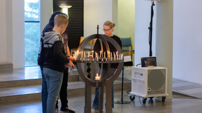 Tre ungdommer står rundt lysgloben og tenner lys i den