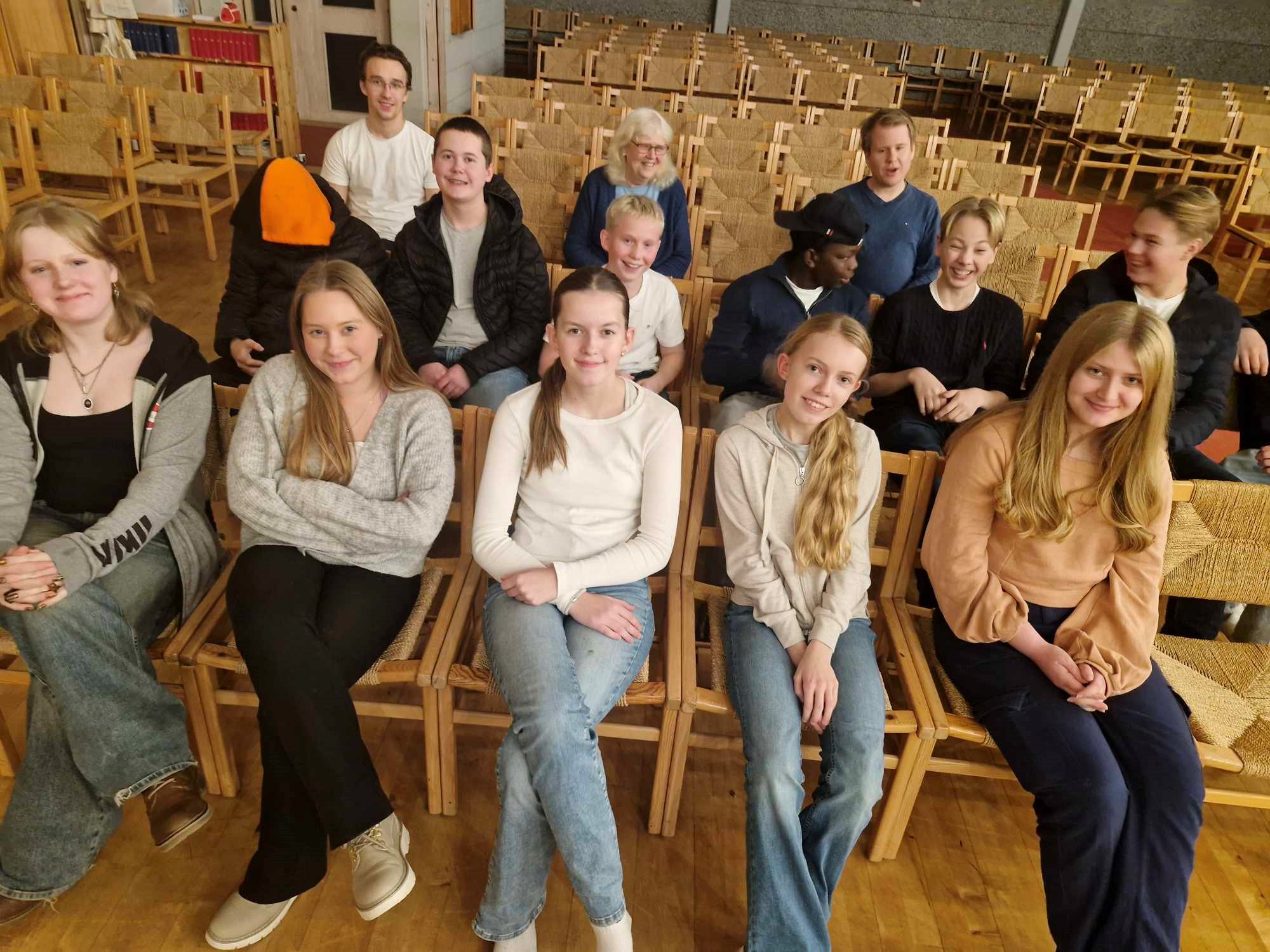 Ungdommer sitter på stolradene i kirken, de smiler til kameraet