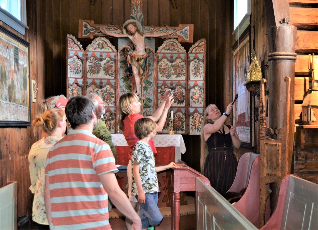 Omviser Marie Veimodet inne i Hedalen stavkirke med en gruppe turister, Foto Linn-Helene Larsen