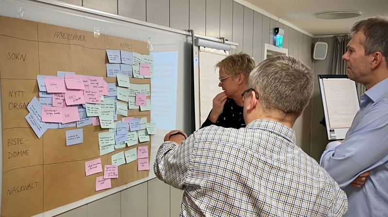Hovedutvalgsmedlemmene Ann Kristin Langeland, Martin Enstad og Torbjørn Backer Hjorthaug i workshop med å plassere notatlapper med oppgaver og ansvar i en ny kirkelig struktur.