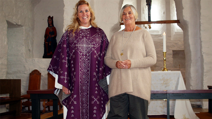 Borgny Farstad Svalastog (til høyre) har laget kirketekstiler til kirker over hele landet. Her sammen med daværende sokneprest Annette Stenseng i Herøy i Dønnes kirke i 2012 ved innvielsen av nytt sett med kirketekstiler. Soknepresten viser messehaklen fra det fiolette tekstil-settet. (Foto: Dagrunn Grønbech)