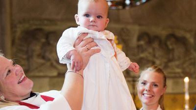 Et barn i dåpskjole løftes opp i kirken
