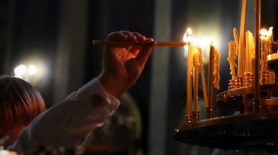 Ei jente strekker seg omm og tenner et lys i et mørkt kirkerom. Lysene er lange og tynne og minner om ortodoks tradisjon.